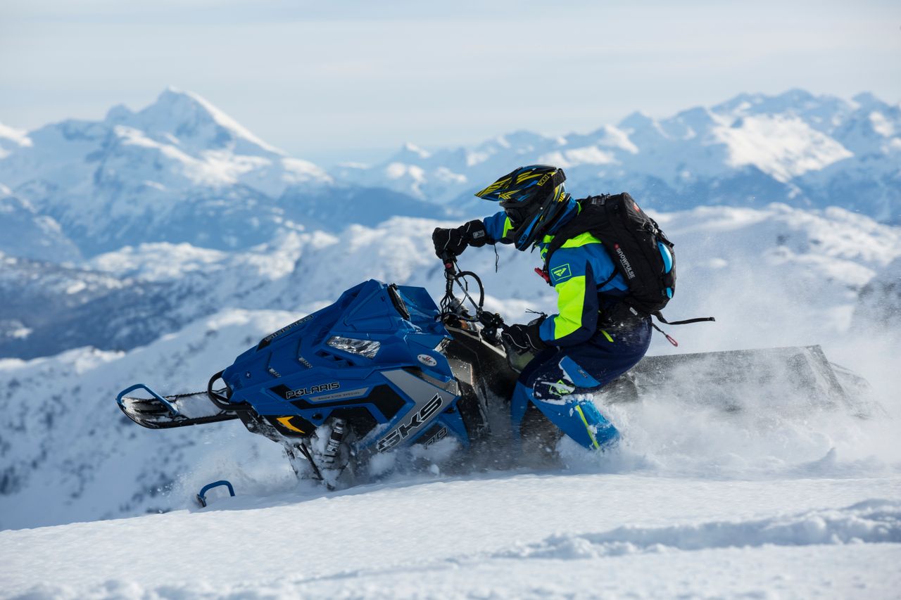 Home Man riding a snowmobile on snowy mountain, showcasing extreme winter sports adventure.